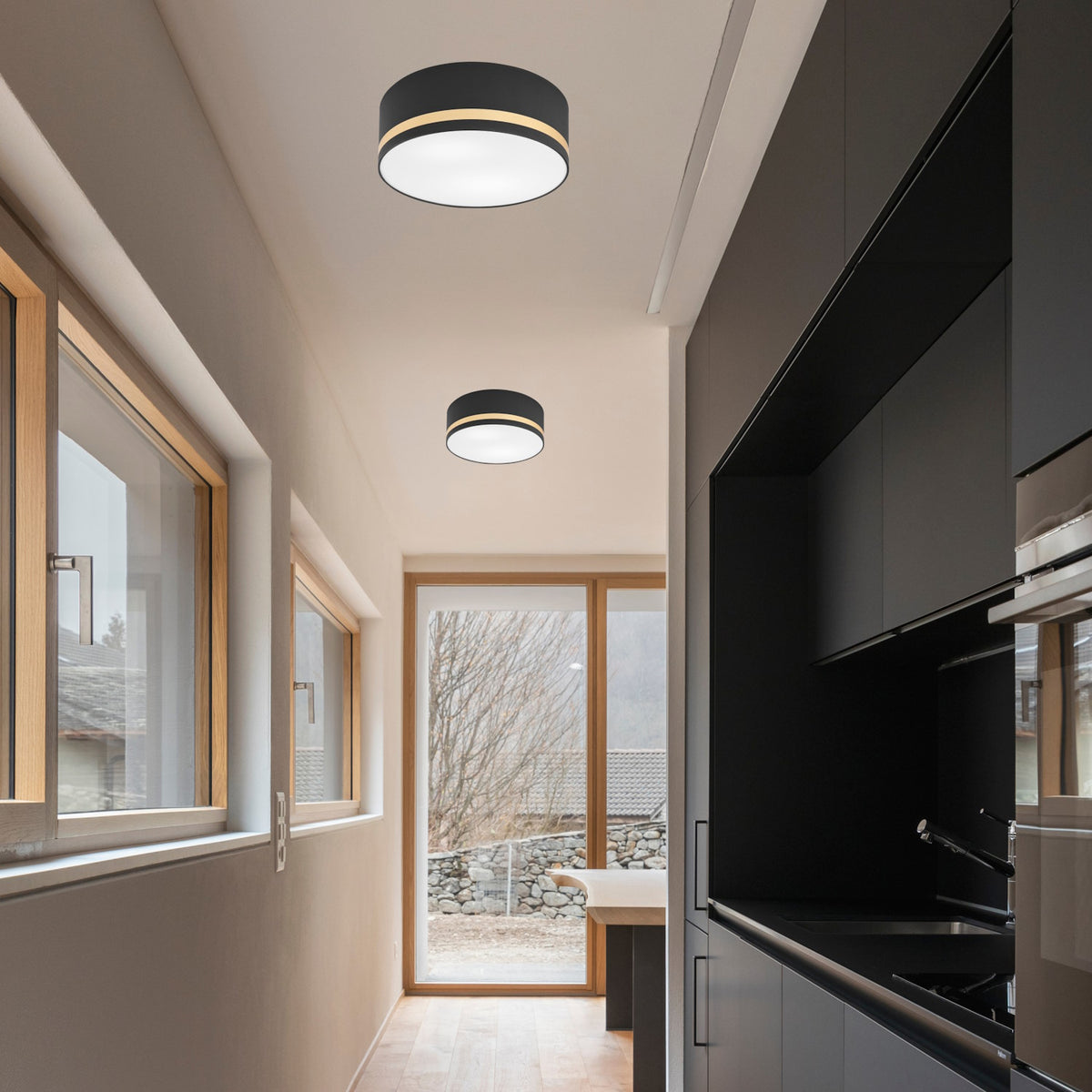 Deux plafonniers identiques éclairent un couloir de cuisine aux meubles noirs.