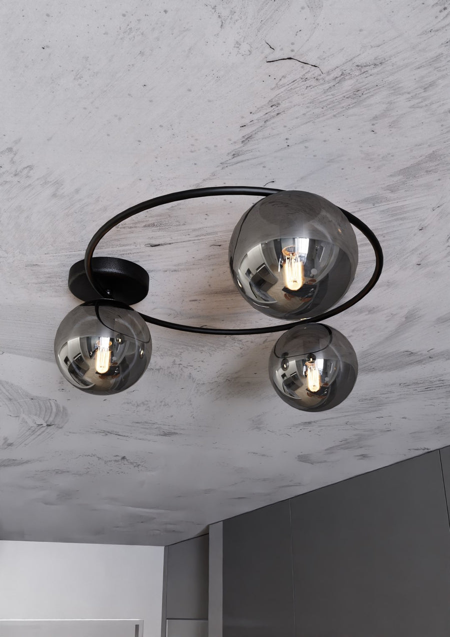 Gros plan sous plafond : cercle noir, trois globes fumés et reflets de la pièce.