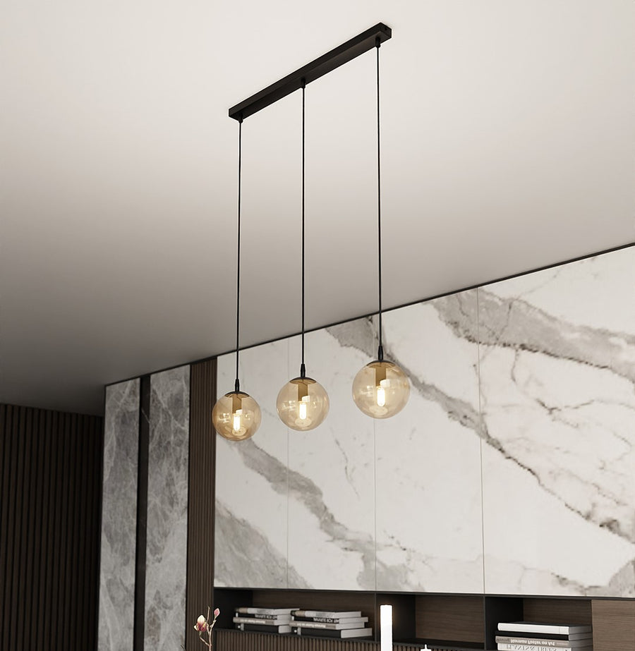 Suspension linéaire noire à trois globes ambrés dans un intérieur moderne et minéral.