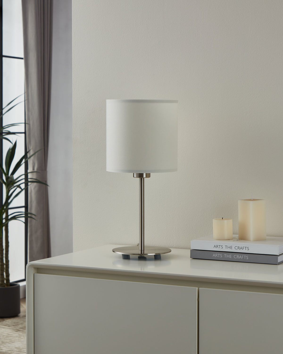 Lampe posée sur un meuble blanc, près de bougies et d'une plante