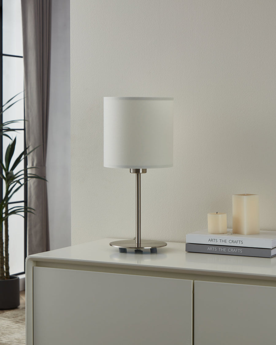 Lampe posée sur un meuble blanc, près de bougies et d'une plante