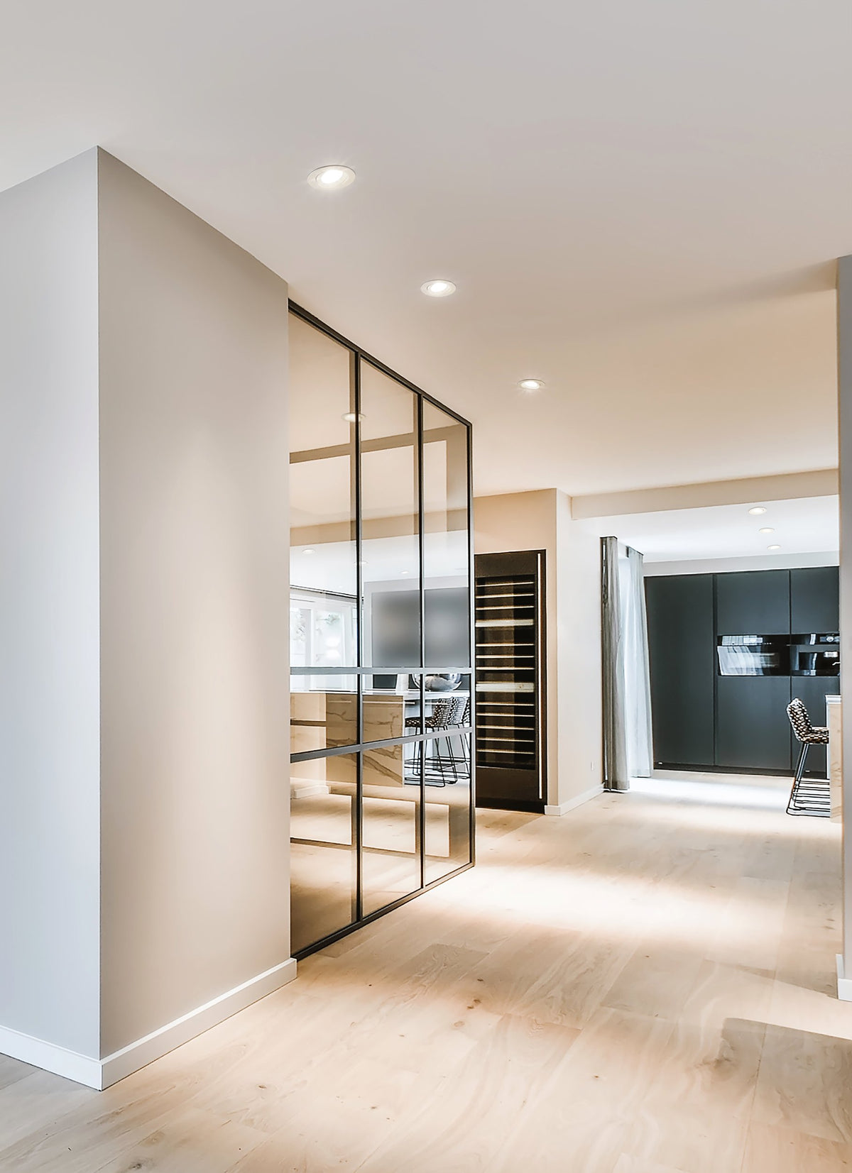 Mise en ambiance de spots encastrés blancs dans un plafond, intérieur moderne avec verrière et cuisine.