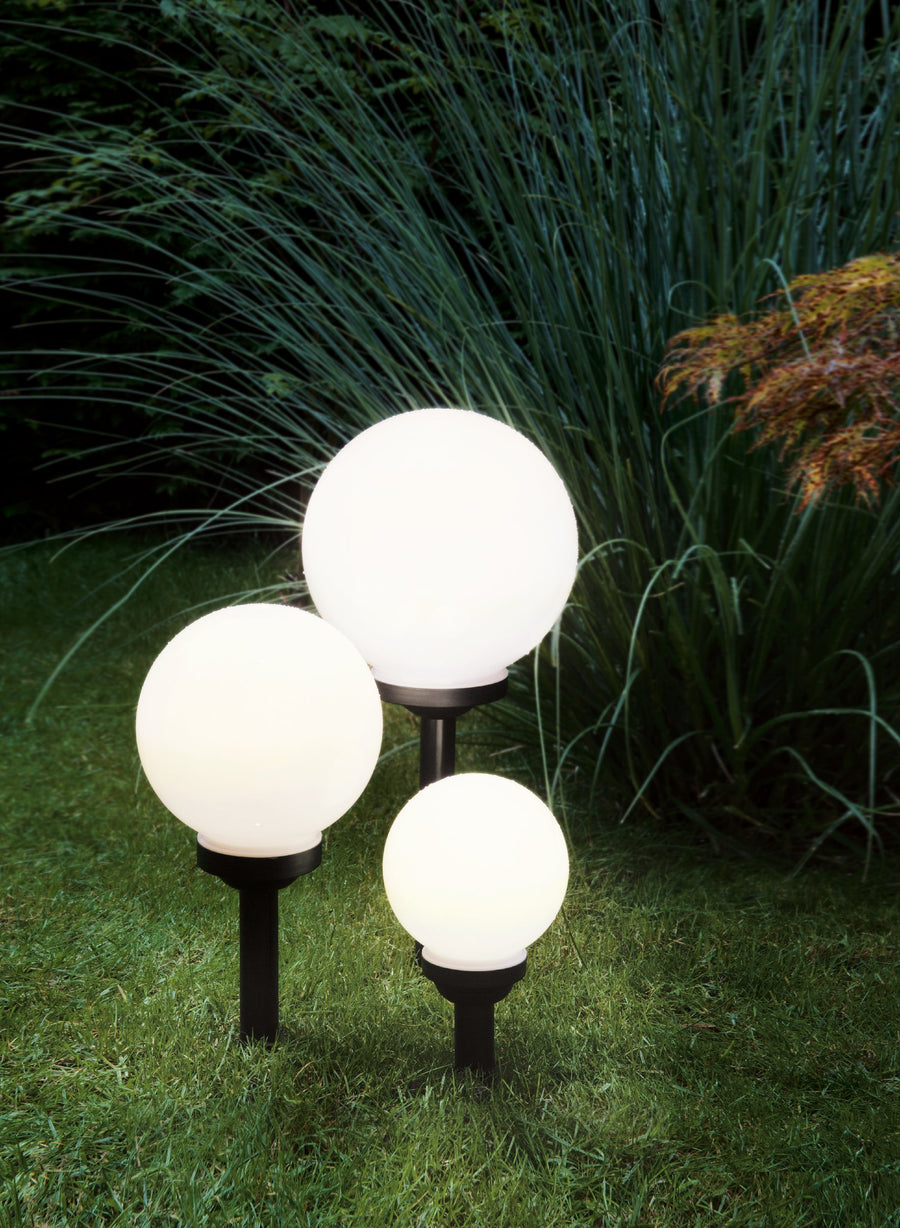 Trois luminaires boule allumés plantés dans l'herbe près de grandes graminées