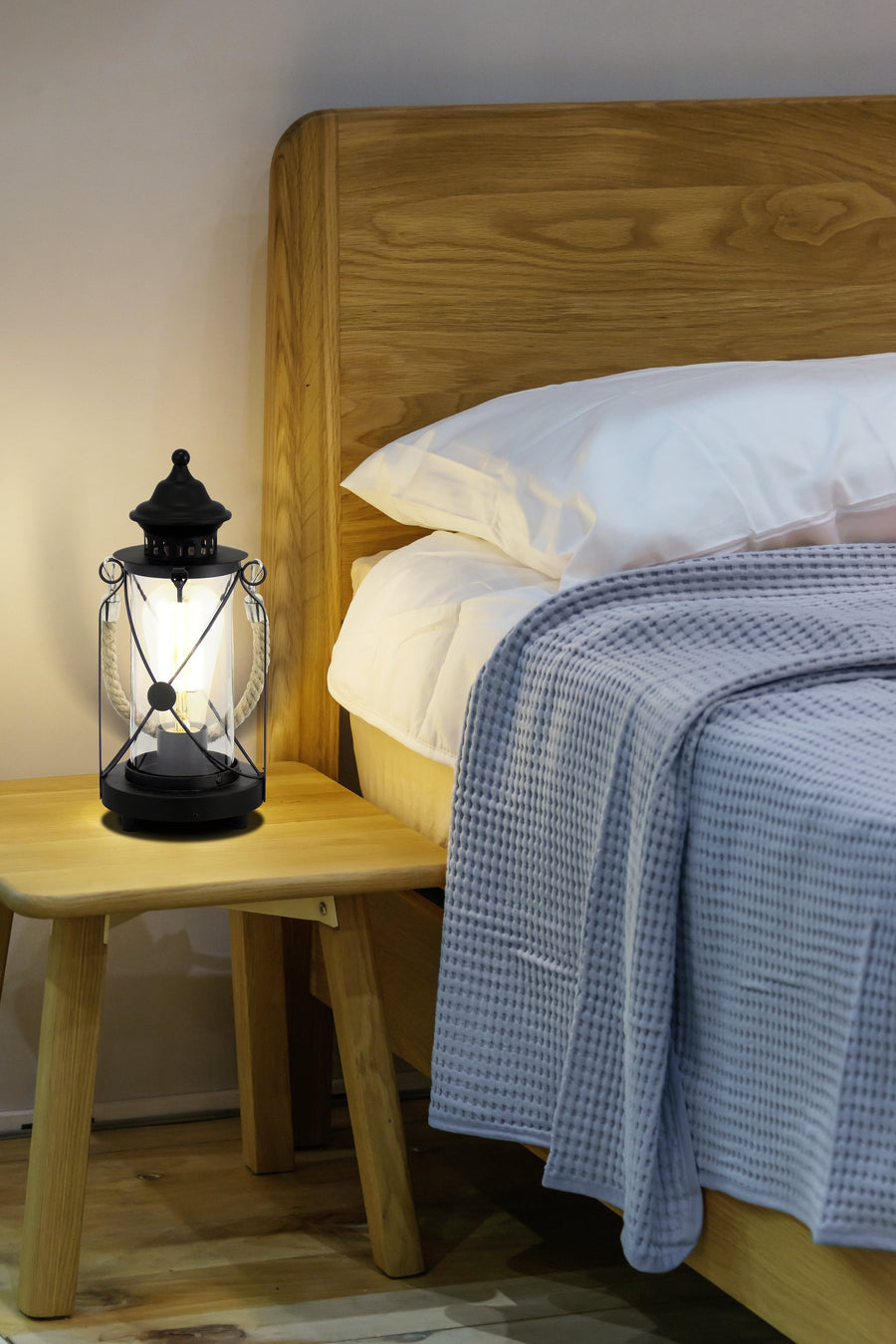 Lampe allumée sur une table de chevet en bois, ambiance chambre