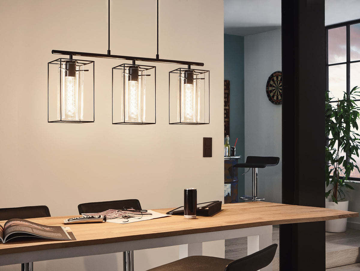 Mise en ambiance au-dessus d'une table en bois, suspension noire allumée dans une pièce de vie.