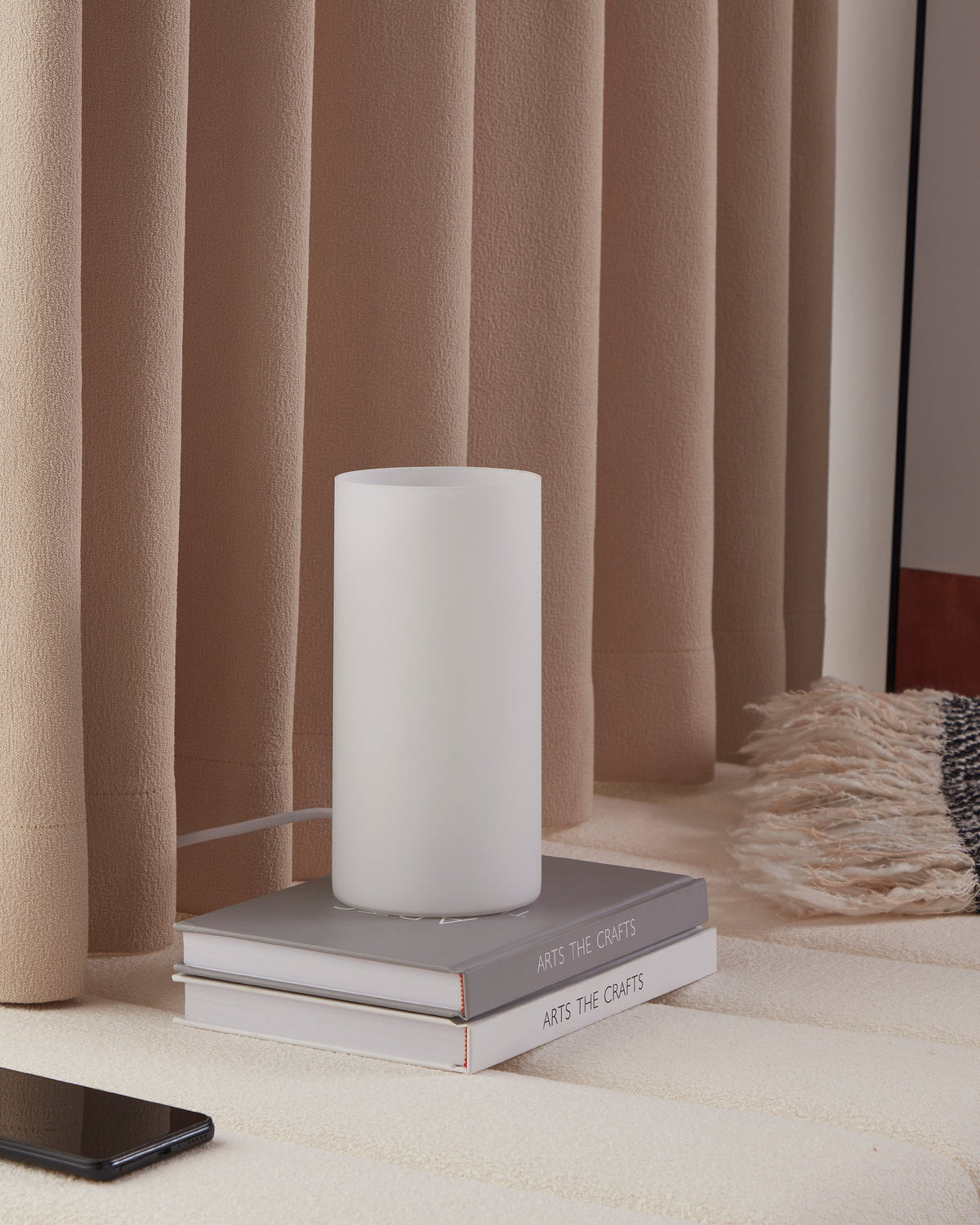 Lampe posée sur des livres devant rideaux beiges, ambiance chaleureuse