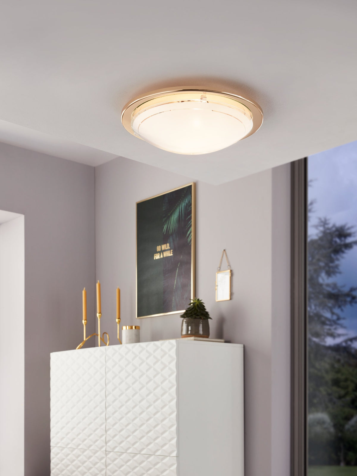 Mise en ambiance : plafonnier allumé au plafond d'un salon, meuble blanc et cadre doré