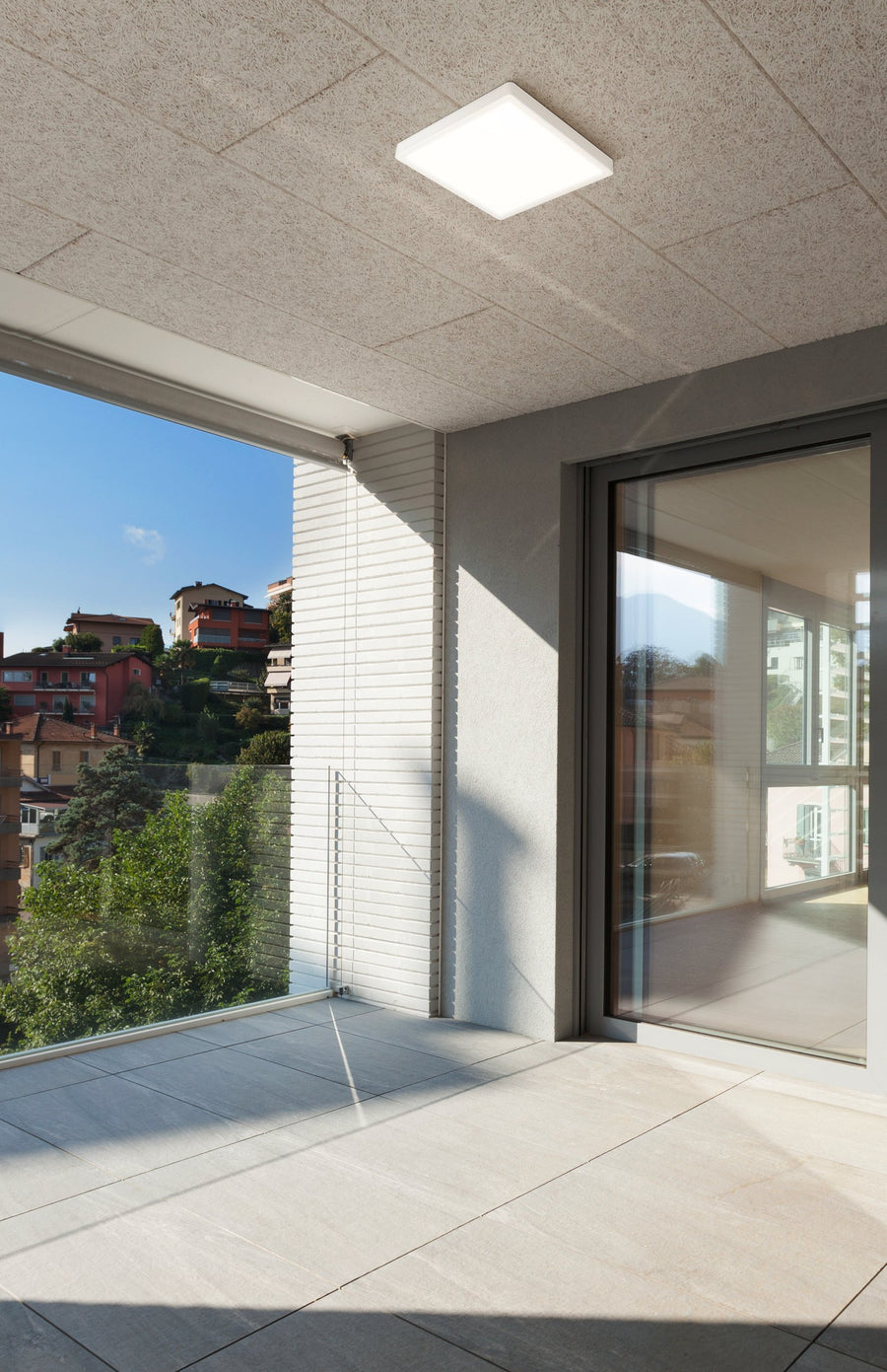 Luminaire carré blanc allumé au plafond d'un balcon avec vue sur les collines.