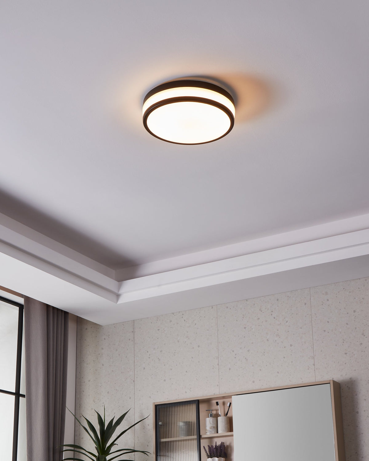 Plafonnier allumé au plafond dans une salle de bains avec meuble et miroir.