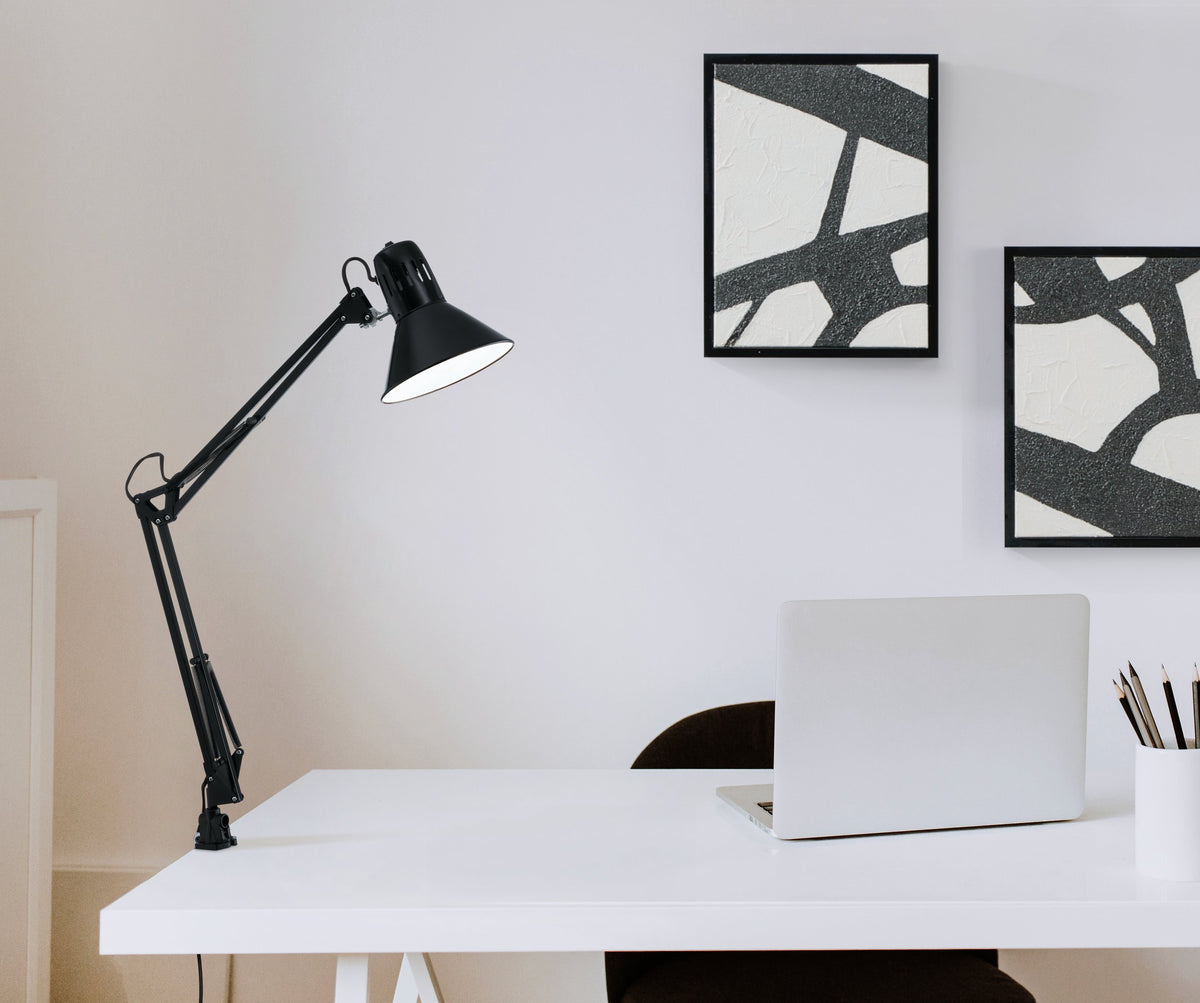 Lampe noire serre-joint installée sur un bureau blanc avec ordinateur et cadres muraux