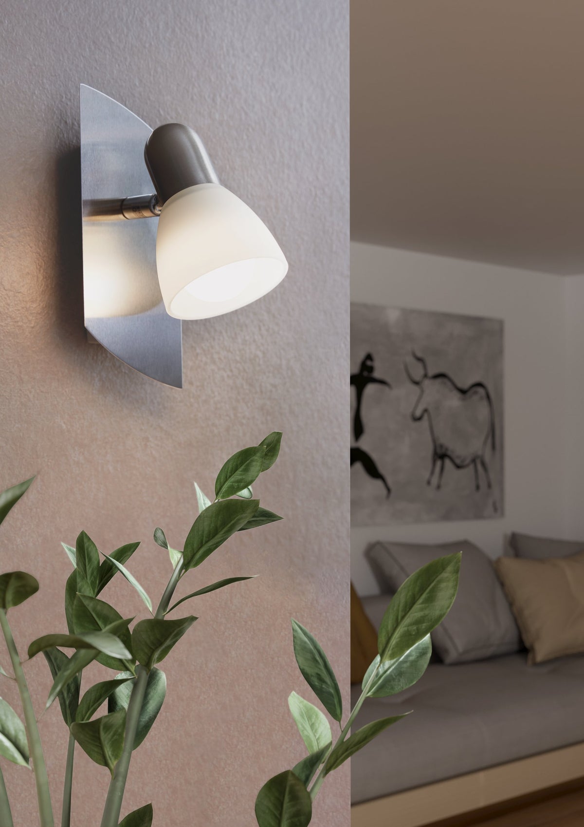 Spot mural allumé sur mur beige avec plante verte et chambre en arrière-plan.