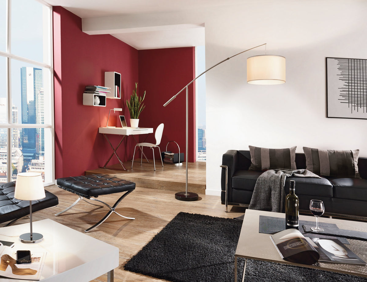 Mise en ambiance salon contemporain avec mur rouge, canapé noir et lampadaire allumé.