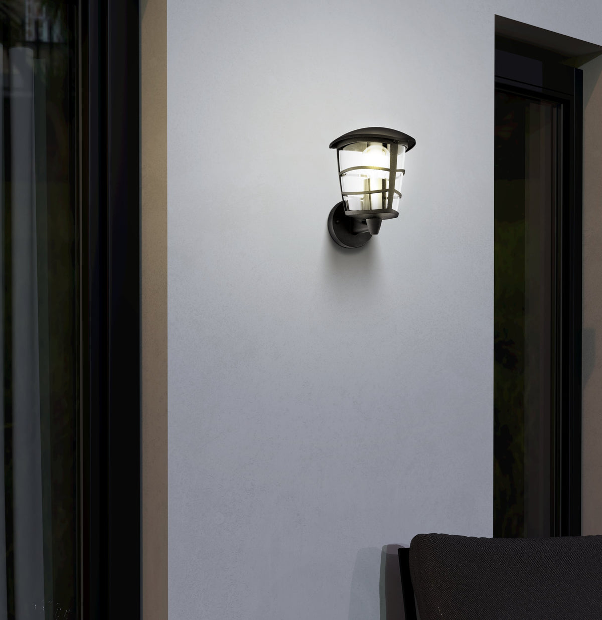 Applique murale noire allumée sur façade claire, mise en ambiance nocturne
