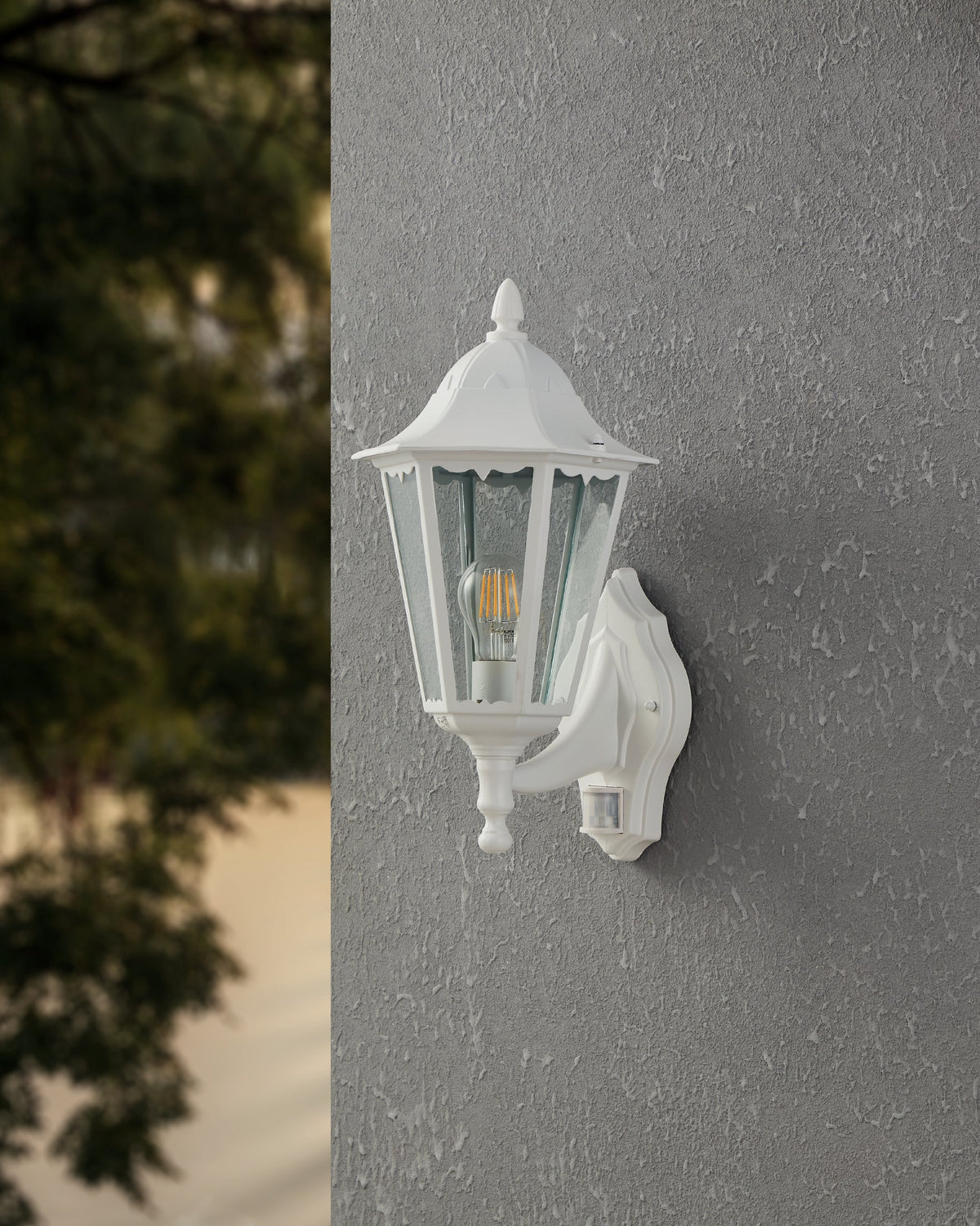 Vue de trois quarts de l'applique blanche éclairée sur une façade grise crépis
