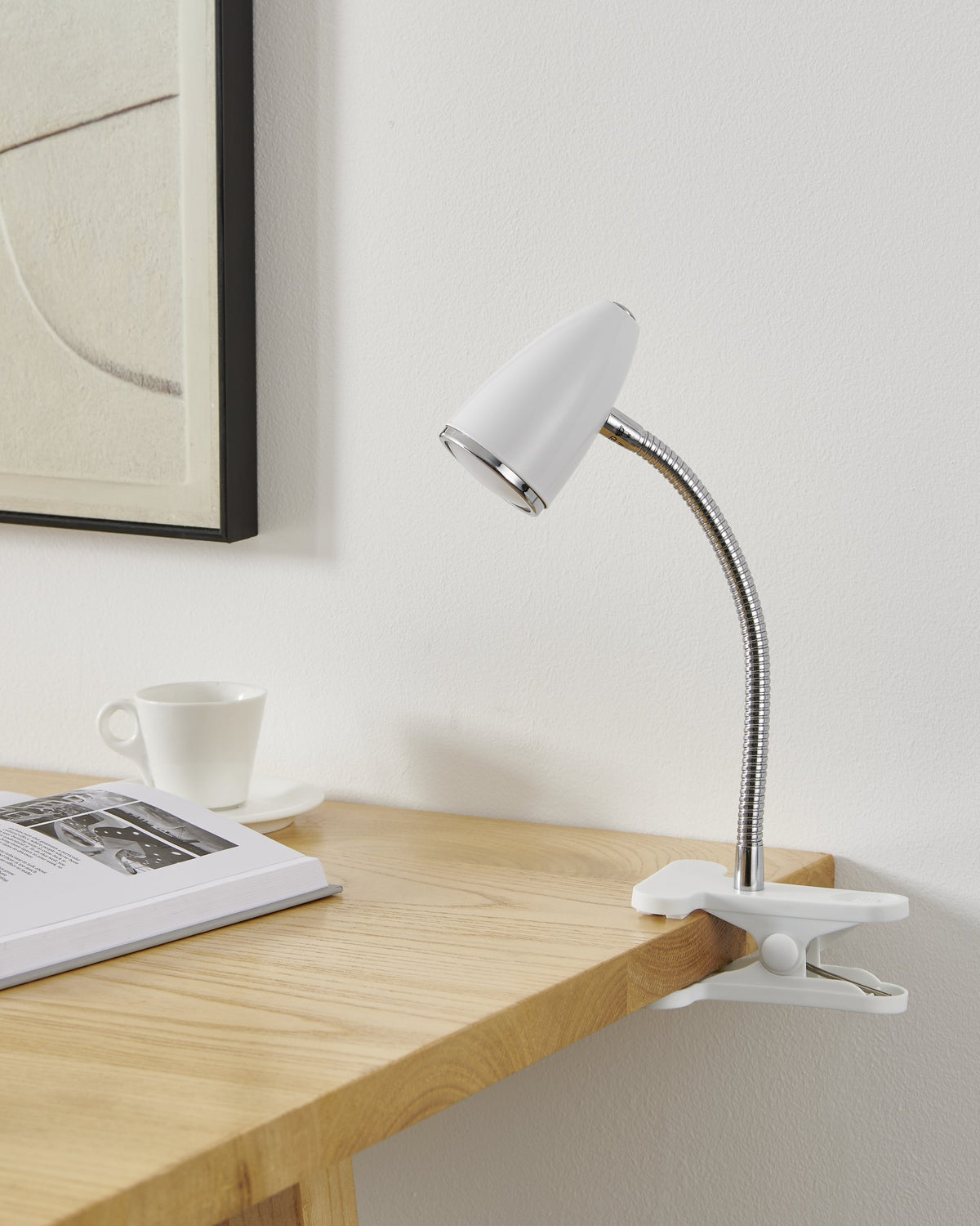 Ambiance bureau chaleureuse avec lampe clipsée, tasse et cadre noir au mur.