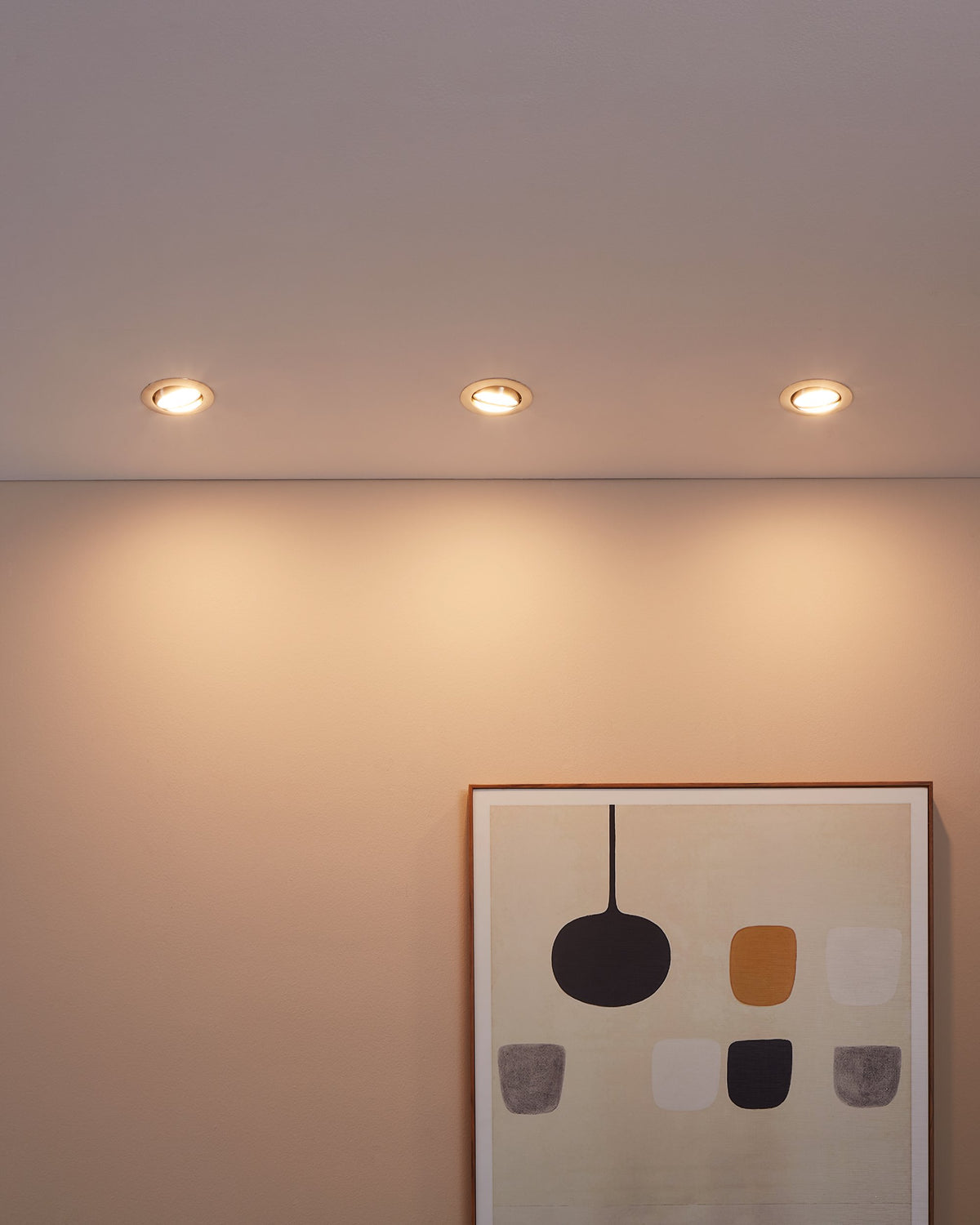 Mise en ambiance de trois spots allumés au plafond éclairant un mur beige