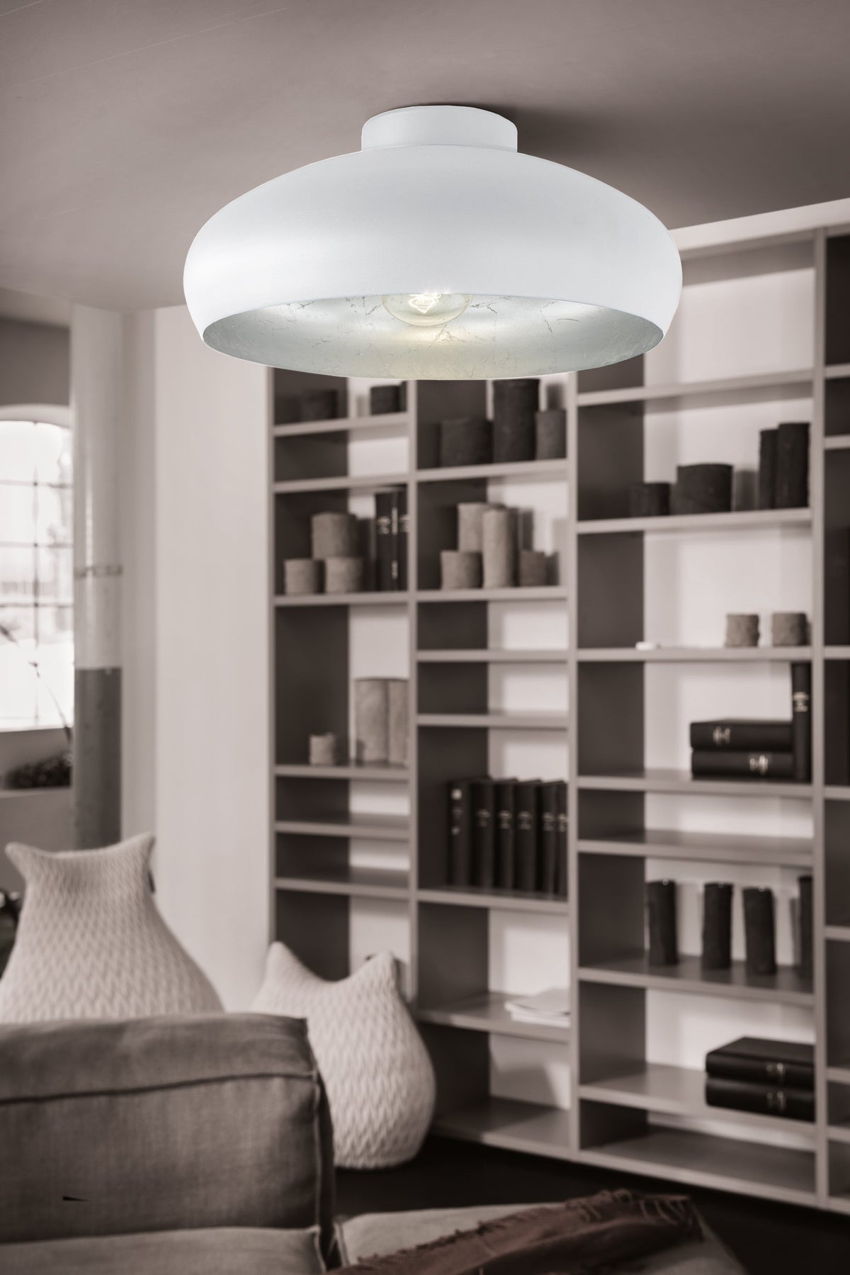 Mise en ambiance du plafonnier blanc allumé devant une grande bibliothèque de salon