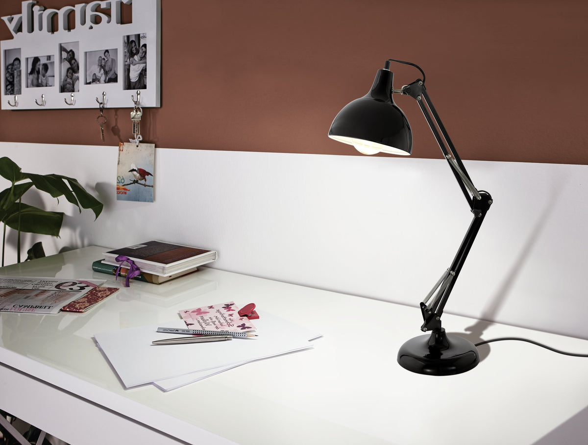Lampe allumée posée sur un bureau blanc, livres et cadre photo en arrière-plan.