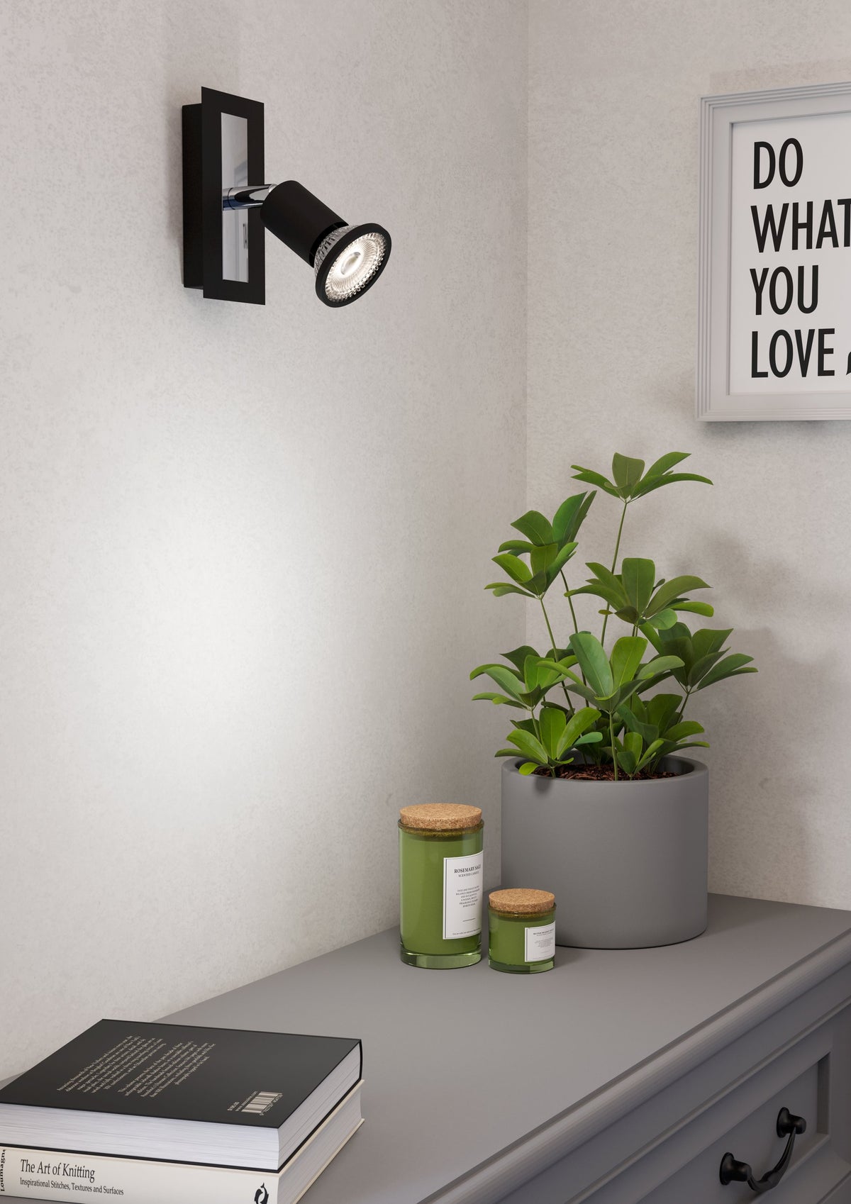 Spot mural allumé au-dessus d'une commode grise, ambiance intérieure avec plante et bougies