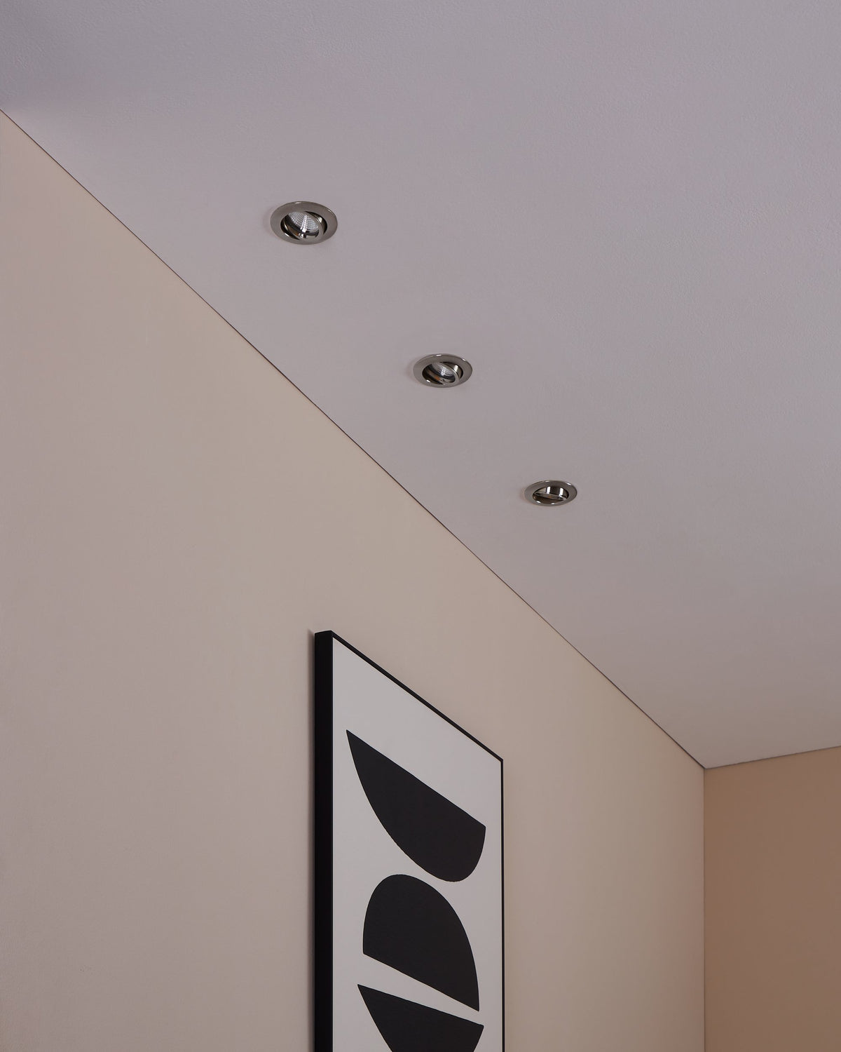 Vue plafond avec trois spots encastrés éteints près d’un cadre mural noir.