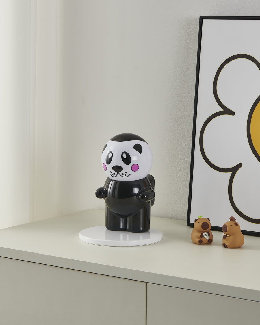 Lampe panda éteinte posée sur un meuble blanc près d'un cadre et de figurines