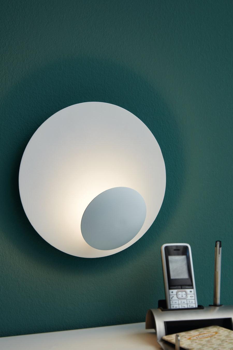 Luminaire mural allumé sur un mur vert foncé au-dessus d'un bureau