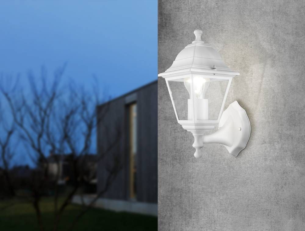 Applique murale blanche allumée, fixée sur un mur gris en extérieur au crépuscule.