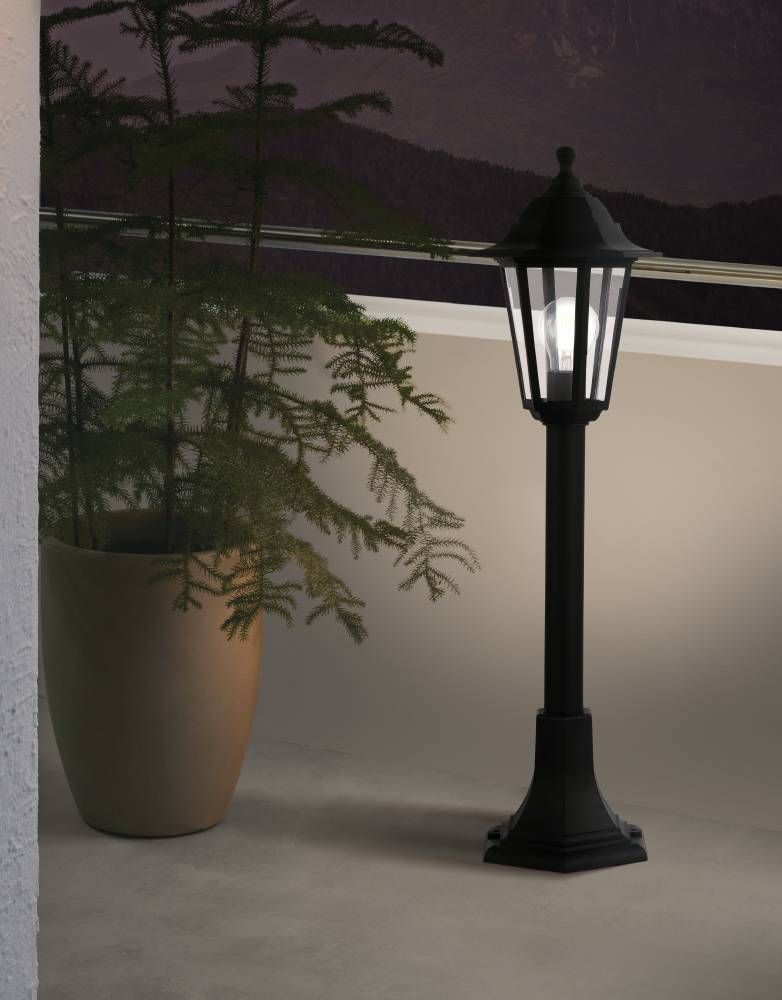 Lampadaire allumé la nuit sur une terrasse, près d'un grand pot et d'un sapin.