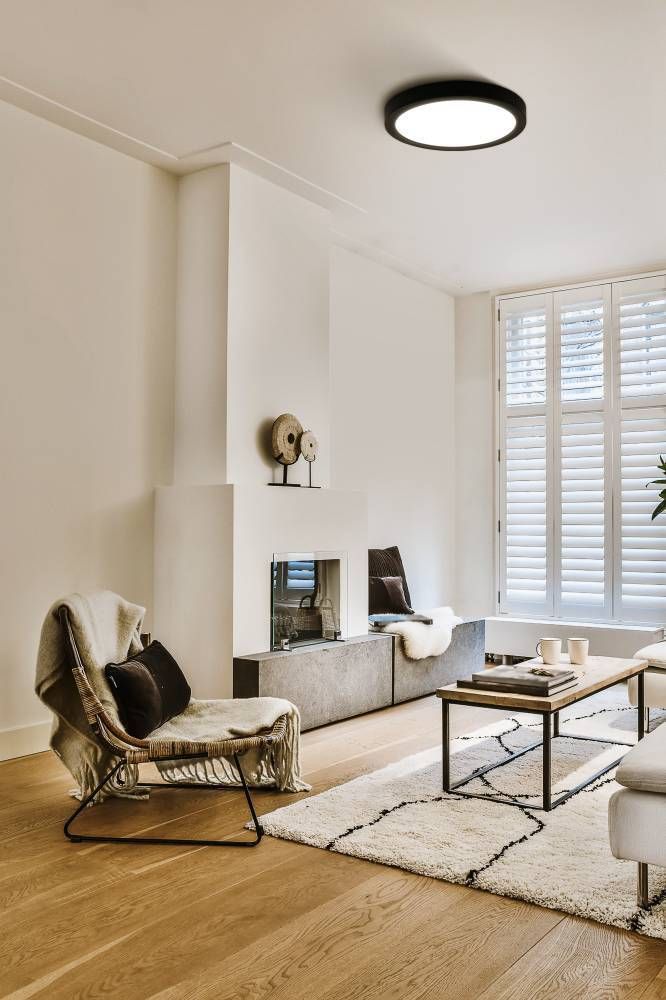 Plafonnier allumé au plafond d'un salon blanc avec fauteuil et cheminée