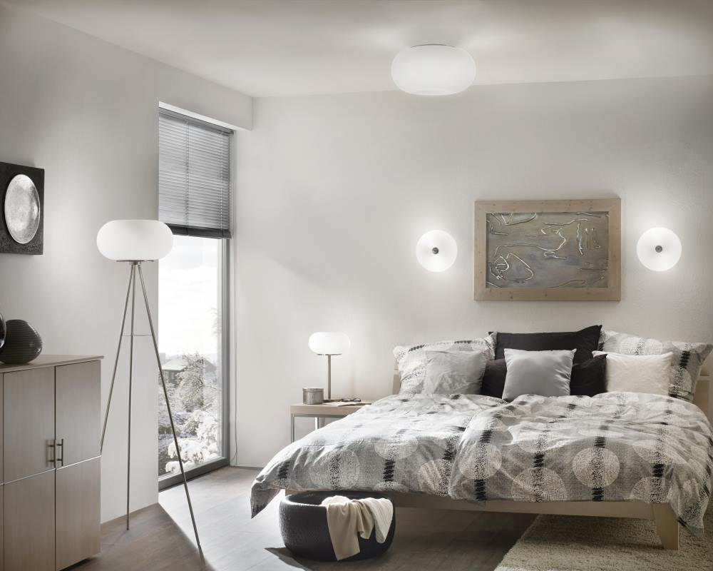 Plafonnier ovale blanc installé au plafond d'une chambre moderne, avec lampes murales et lampadaire.
