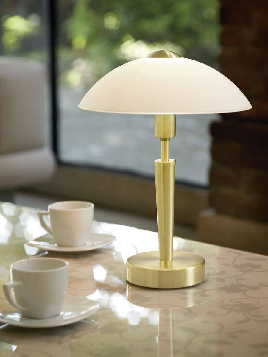 Lampe à poser laiton allumée posée sur une table avec deux tasses