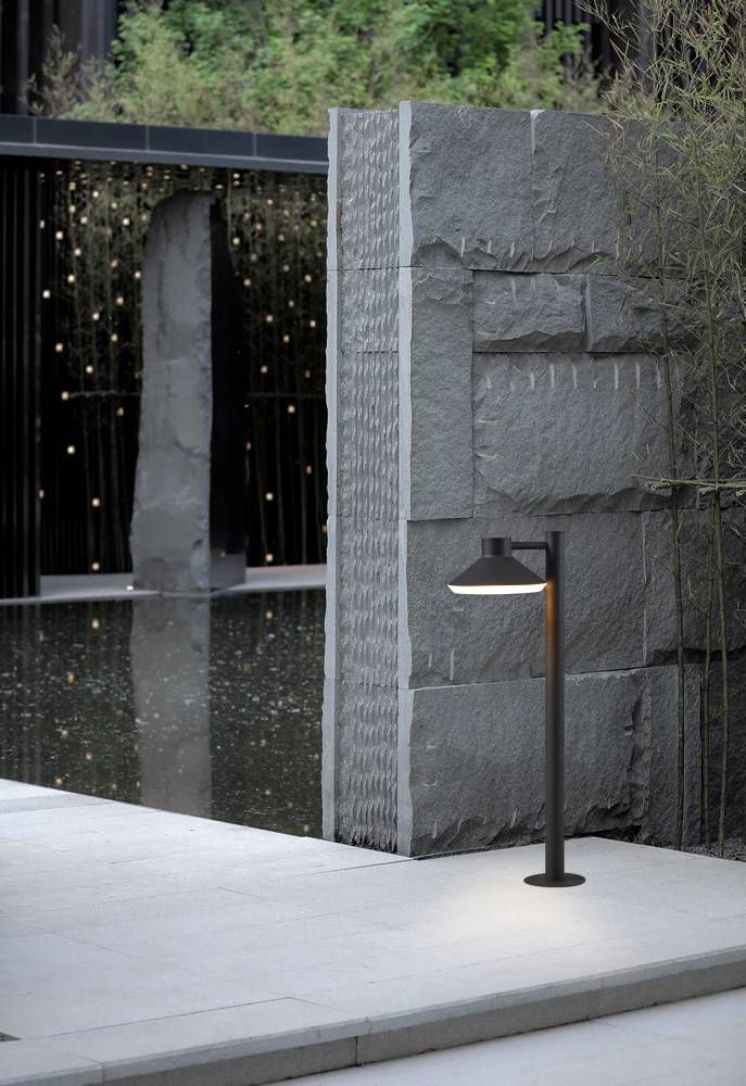 Mise en ambiance du lampadaire éclairé devant un mur de pierre et un bassin