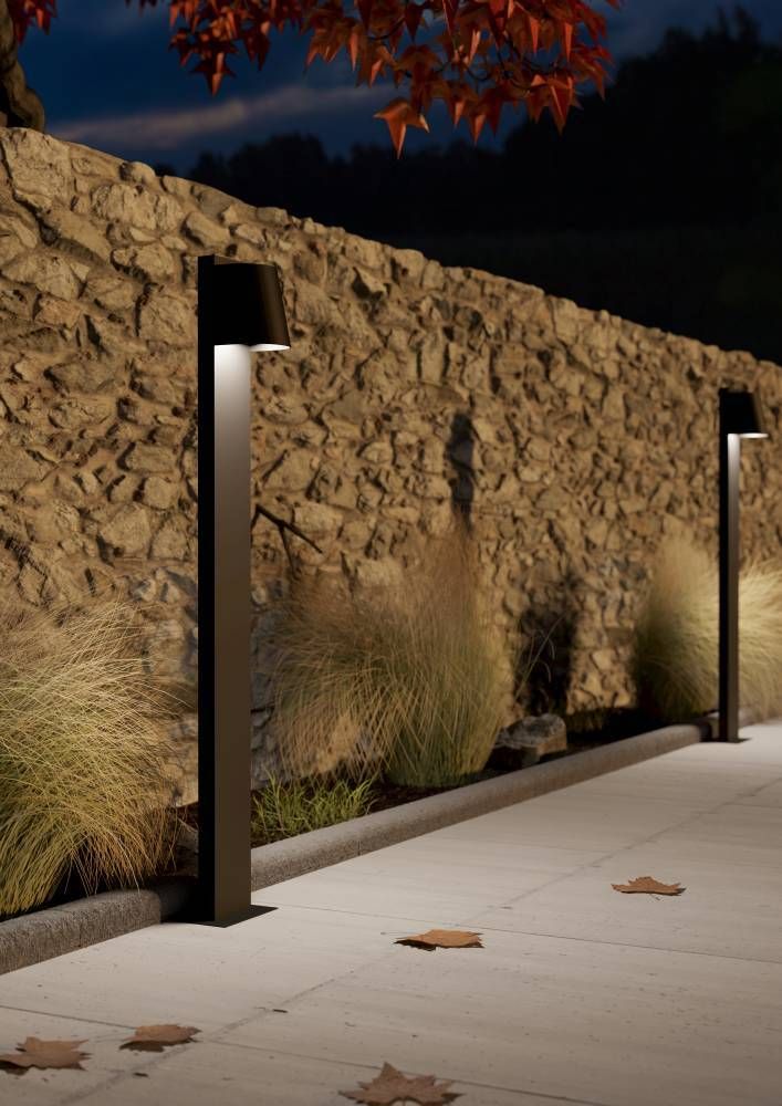Mise en ambiance nocturne de deux bornes noires le long d'un mur en pierre