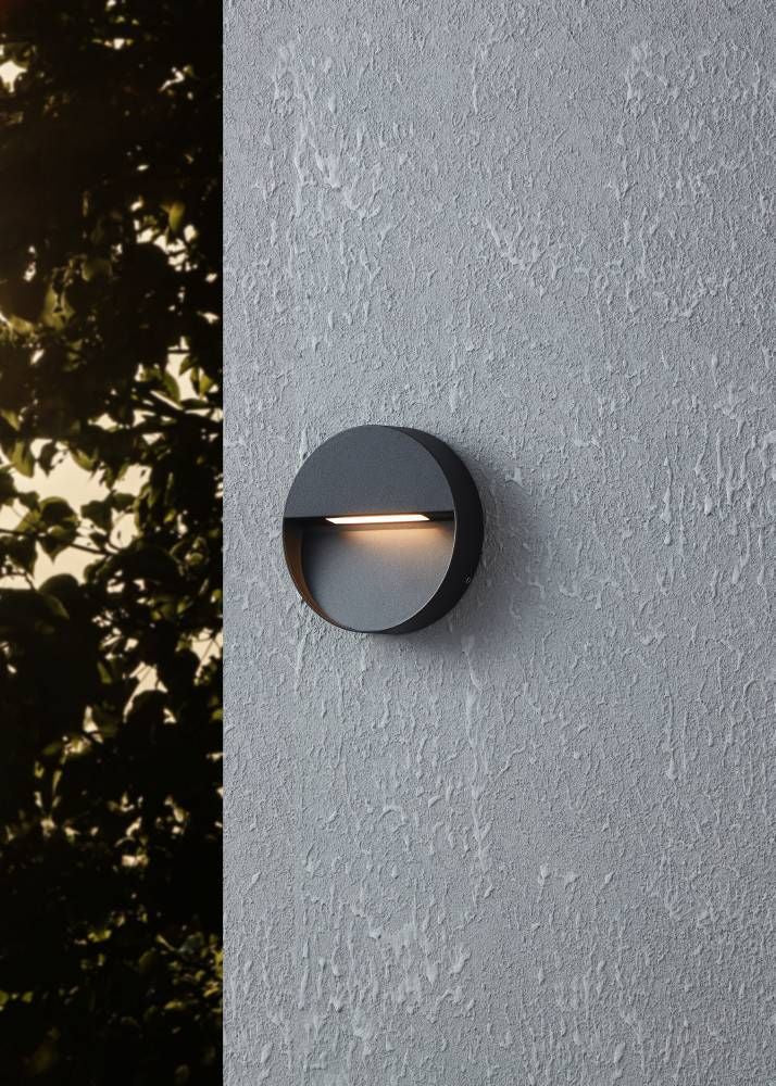 Applique murale noire installée sur un mur crépis, éclairage indirect vers le bas.