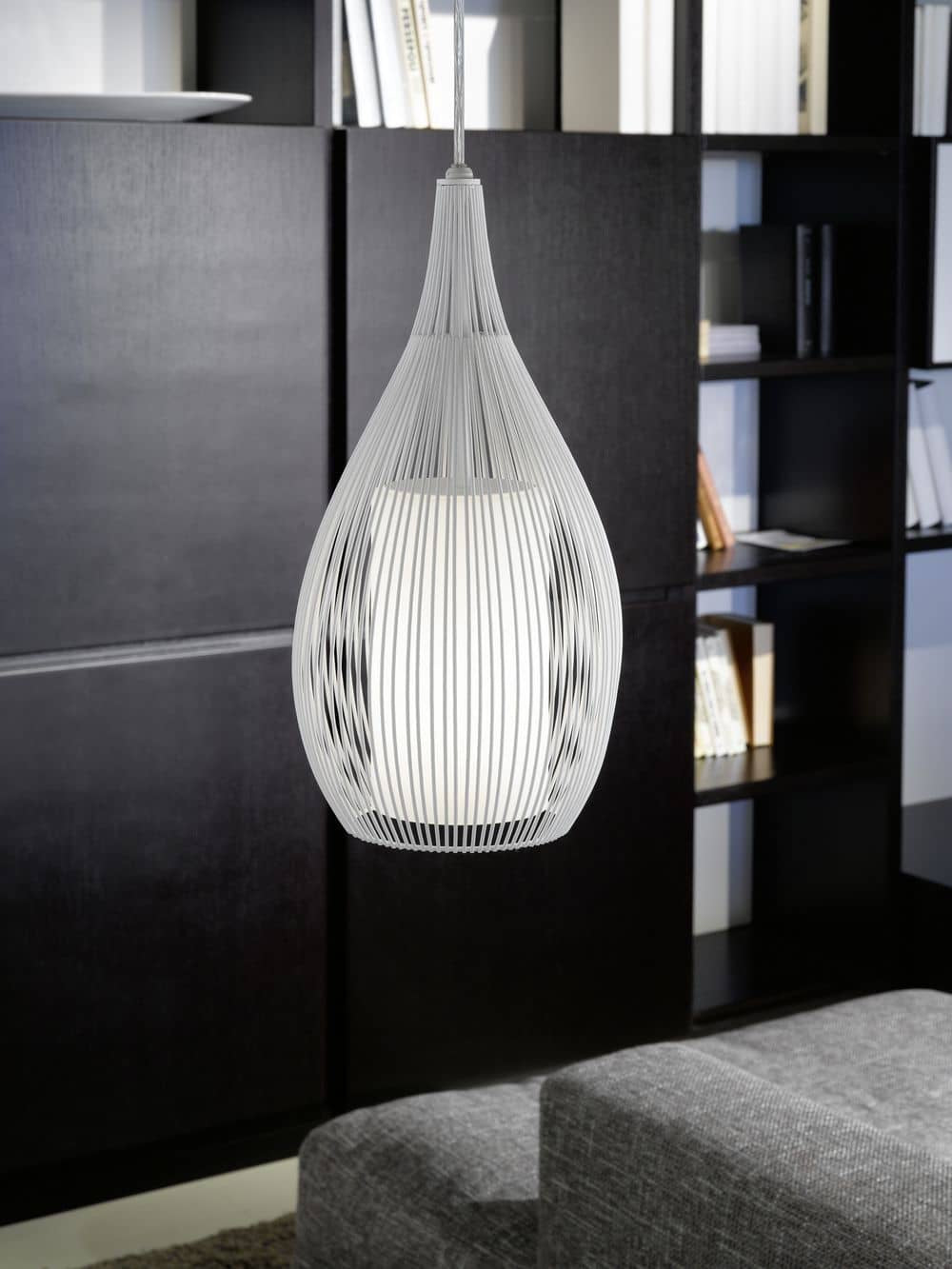 Mise en ambiance du luminaire allumé dans un intérieur sombre avec bibliothèque et canapé.