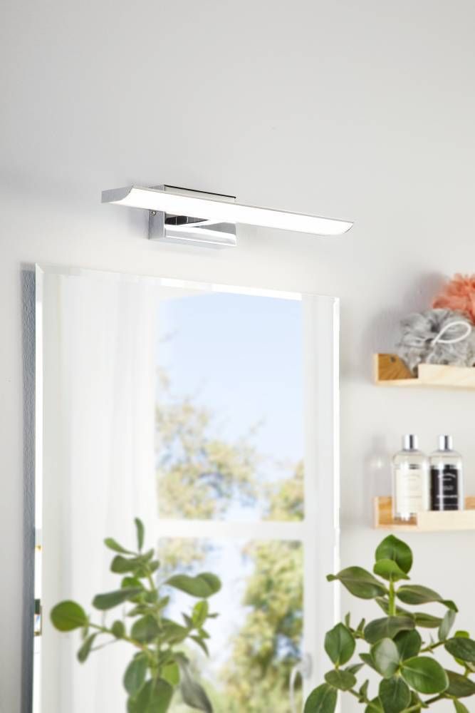 Luminaire mural au-dessus d'un miroir dans une salle de bain claire avec plantes