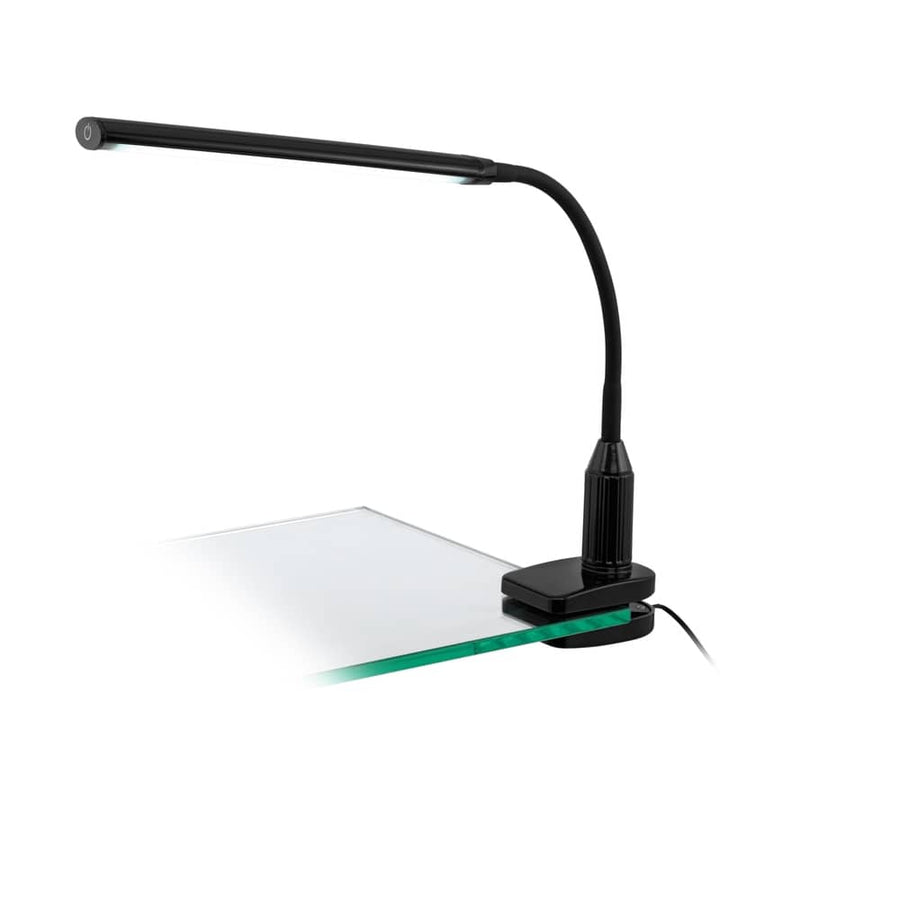 Lampe noire pincée sur un bureau en verre, vue de trois quarts sur fond blanc
