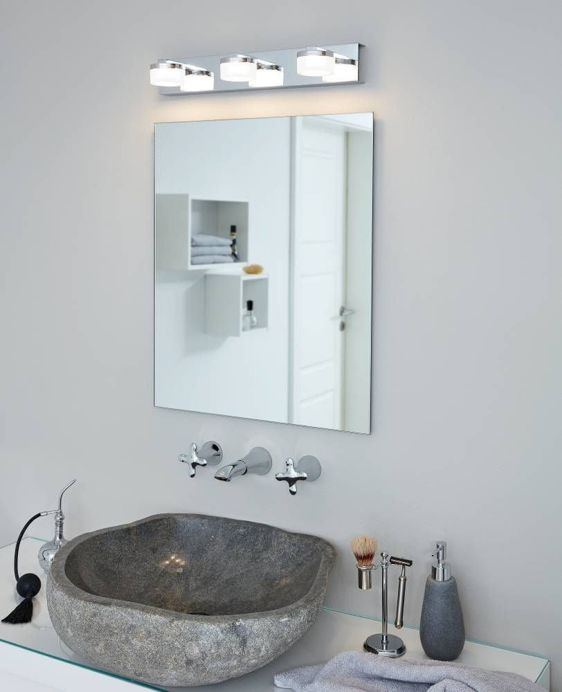 Applique murale à trois lumières éclairant un miroir et une vasque dans une salle de bain.