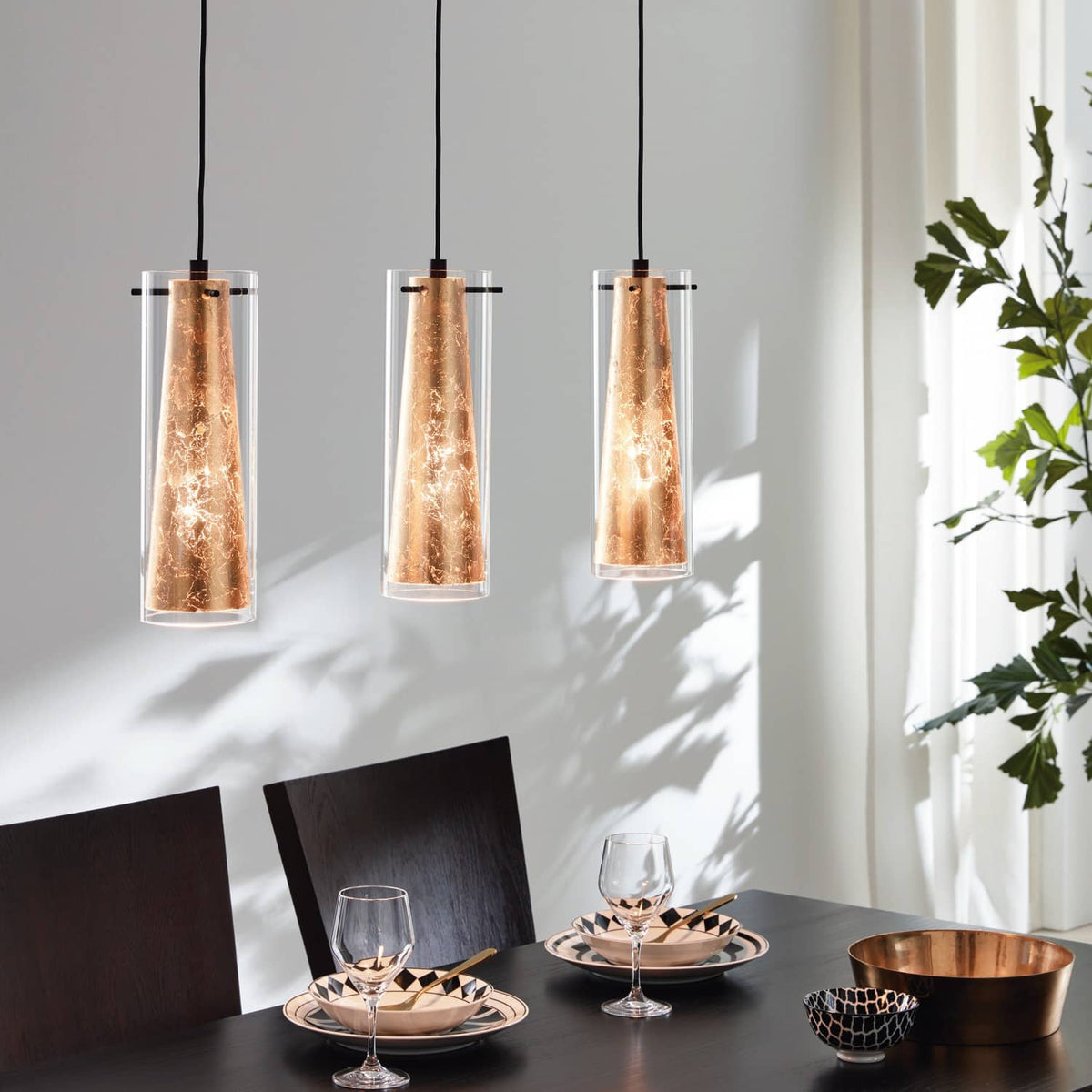 Suspension dorée et transparente au-dessus d'une table dressée, ombres de plantes, ambiance moderne