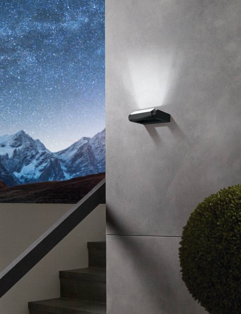 Applique noire fixée sur un mur gris, éclairant vers le haut, mise en ambiance nocturne.