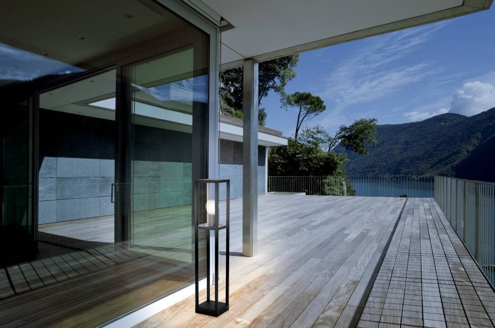 Lampadaire noir sur terrasse en bois devant une baie vitrée, lac et montagnes au loin