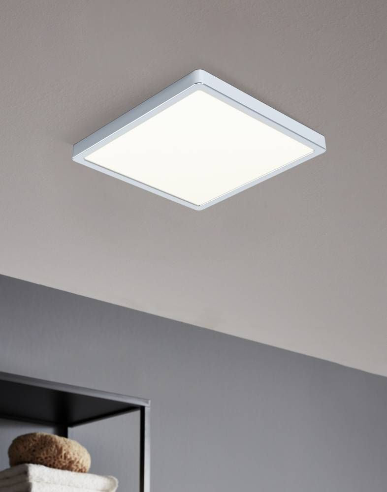 Plafonnier carré allumé, installé au plafond, éclairant une pièce grise avec étagère.