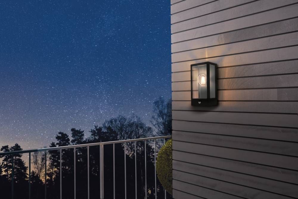 Mise en ambiance nocturne de l'applique allumée sur une façade à lames, ciel étoilé