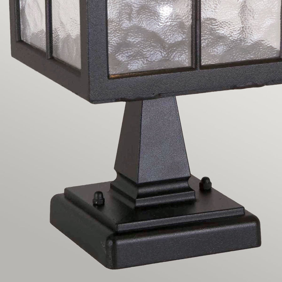Détail de la base carrée noire avec vis de fixation et socle mouluré.