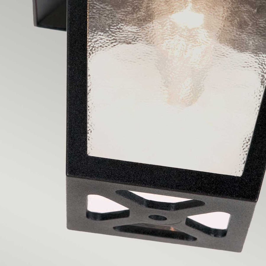 Bas du luminaire montrant découpes en croix et vis de fixation noire.