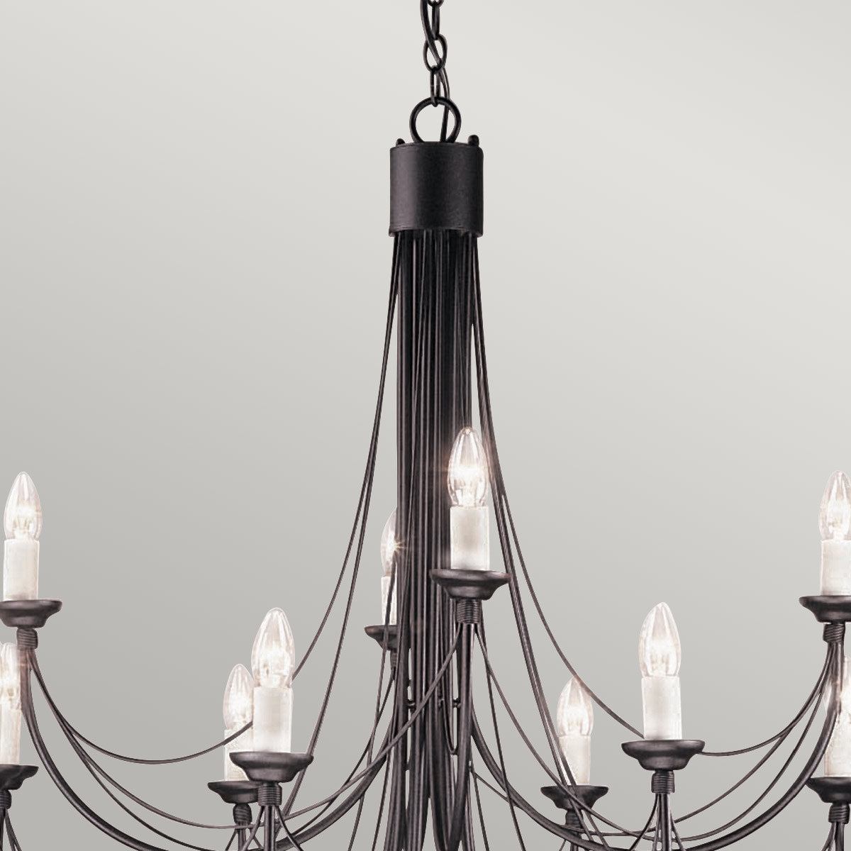 Détail du haut du lustre : chaîne, corps central noir et premières ampoules allumées.