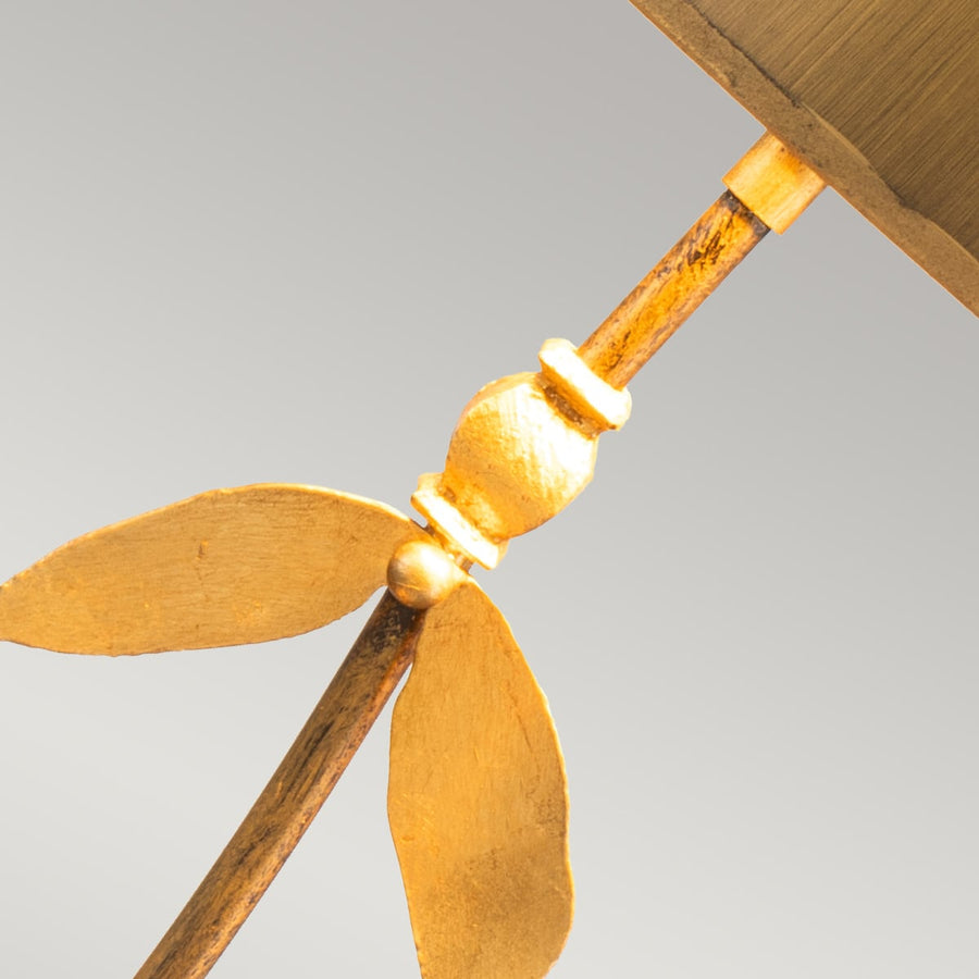 Gros plan du milieu du pied : nœud doré et deux feuilles métalliques texturées.