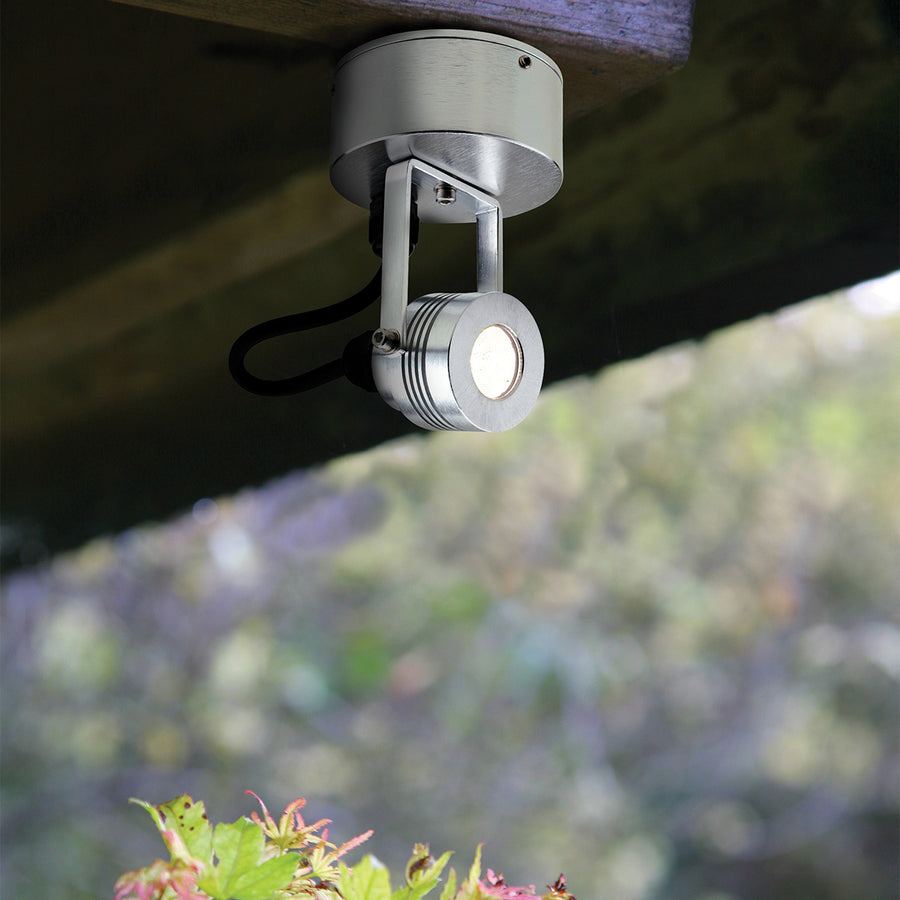 Spot en aluminium fixé sous une poutre en bois, orienté vers le bas dans un jardin