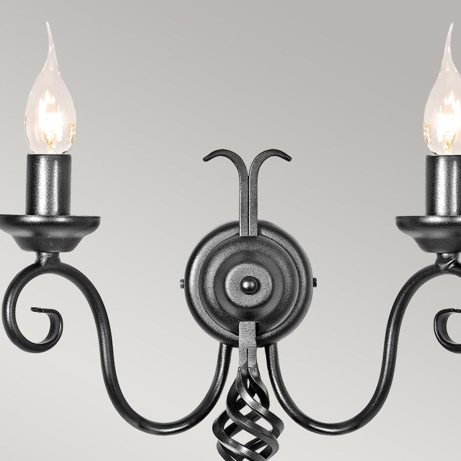 Détail des deux bras recourbés avec bougies et ampoules allumées sur fond gris.