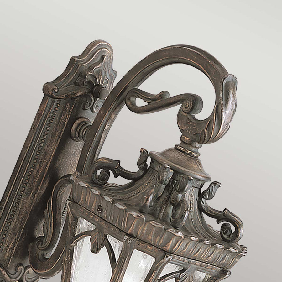 Détail du bras recourbé et des volutes ornementées en métal vieilli de l'applique.